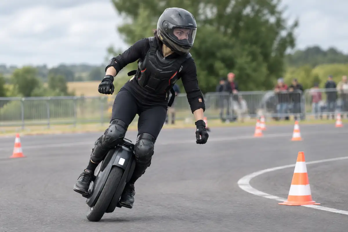 Pilote en casque intégral négociant un virage sur circuit lors d’une course de monoroue électrique.