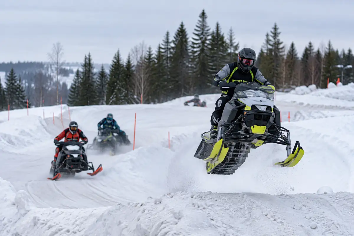 Course de snocross sur un circuit enneigé : un pilote en motoneige franchit une bosse devant d’autres concurrents.