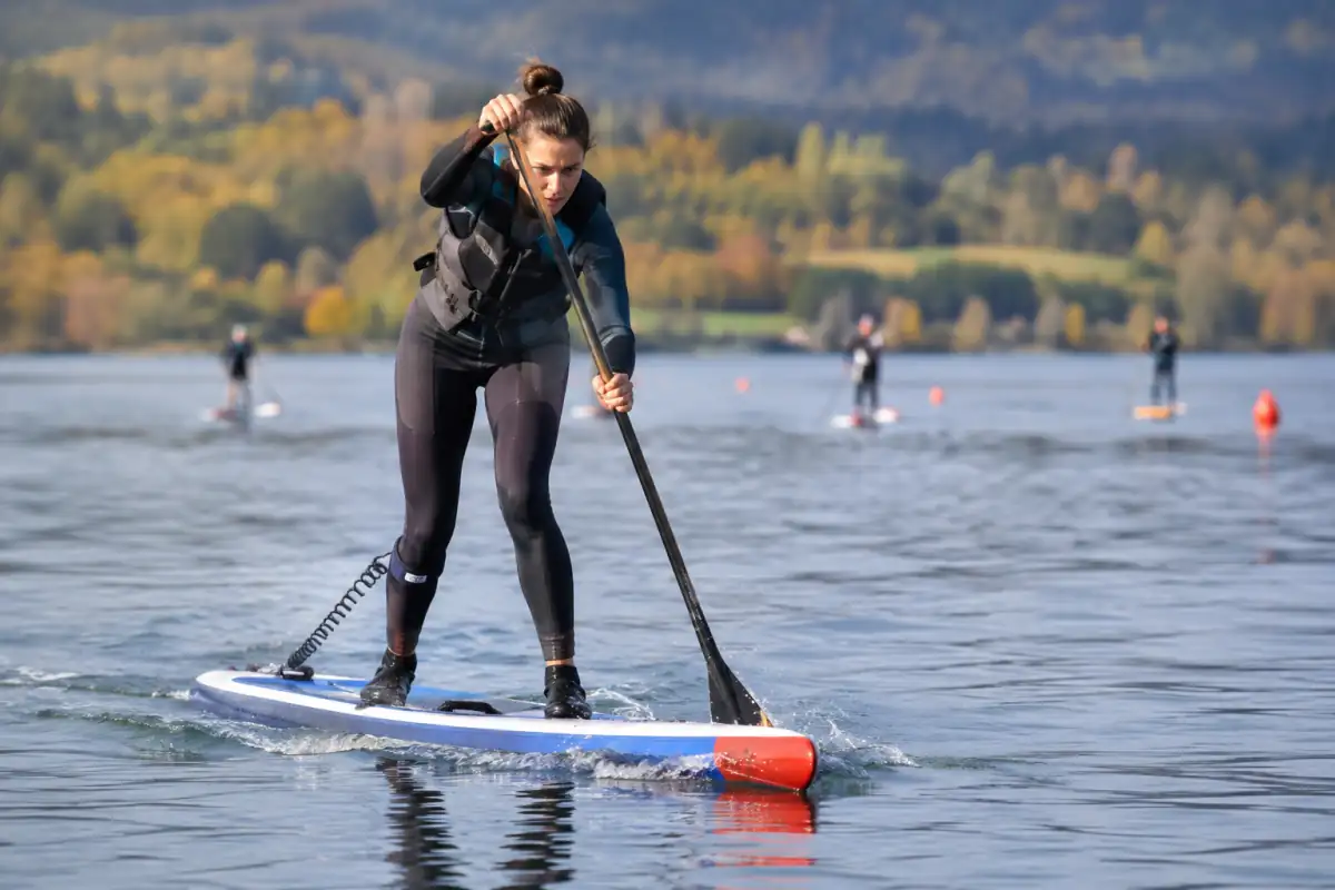 Pagayeur en course de stand up paddle sur une planche longue, au milieu d’un parcours balisé sur un lac.