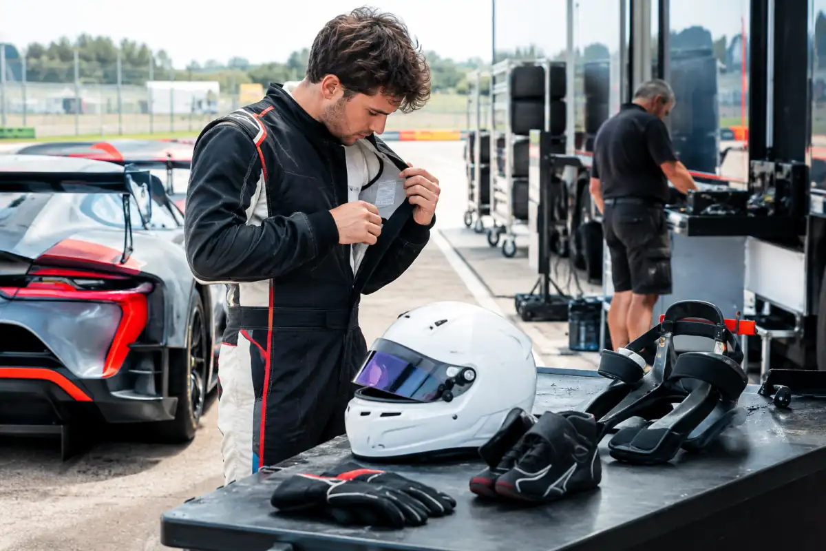 Pilote amateur vérifiant casque, combinaison, gants et dispositif FHR près d’une voiture GT avant une journée de circuit.