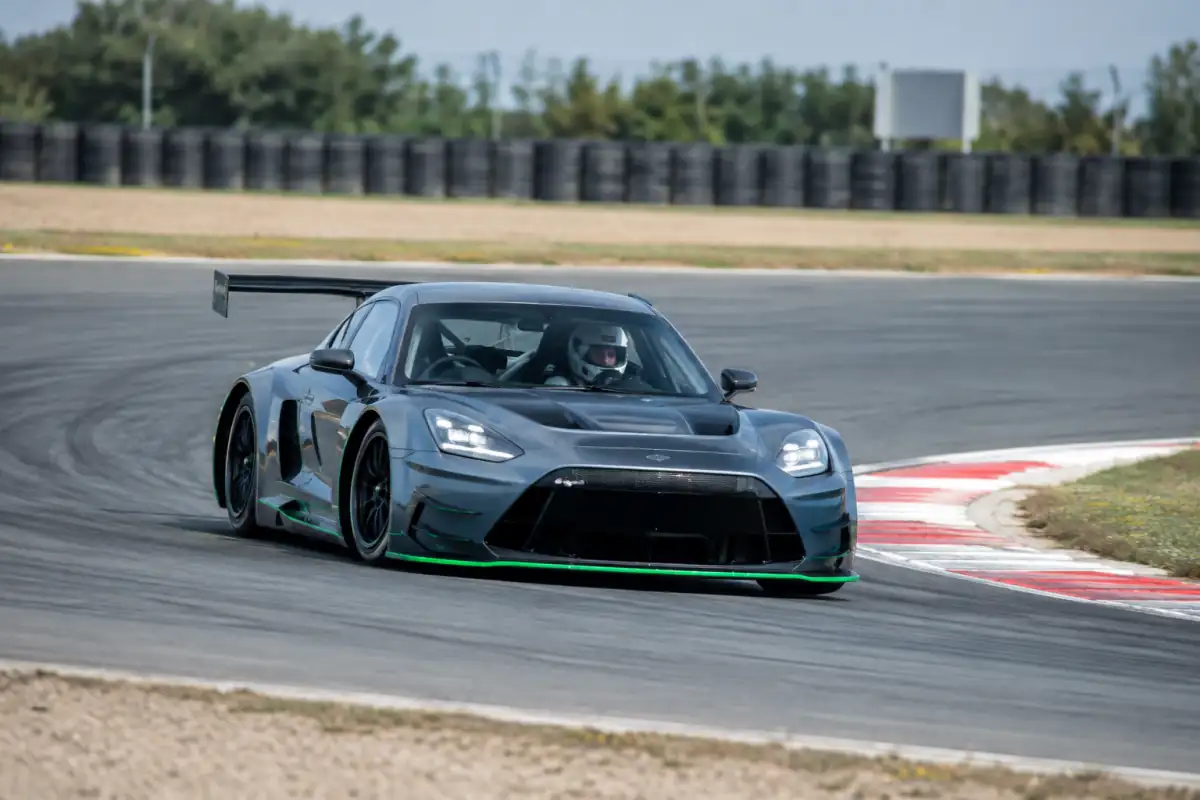 Une voiture GT suit une trajectoire régulière en virage sur circuit, tandis que le pilote regarde vers la sortie.