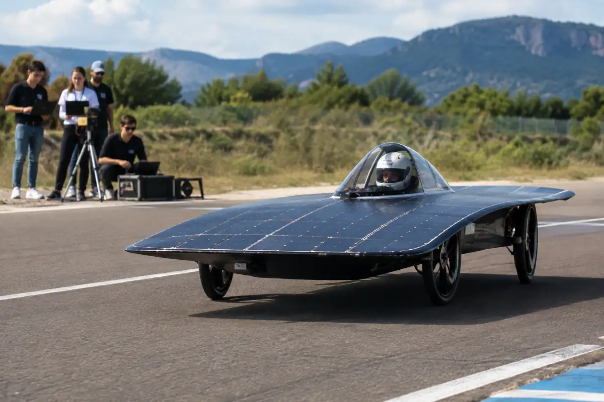 Prototype de voiture solaire piloté sur circuit fermé, avec ses panneaux photovoltaïques et une équipe technique en bord de piste.