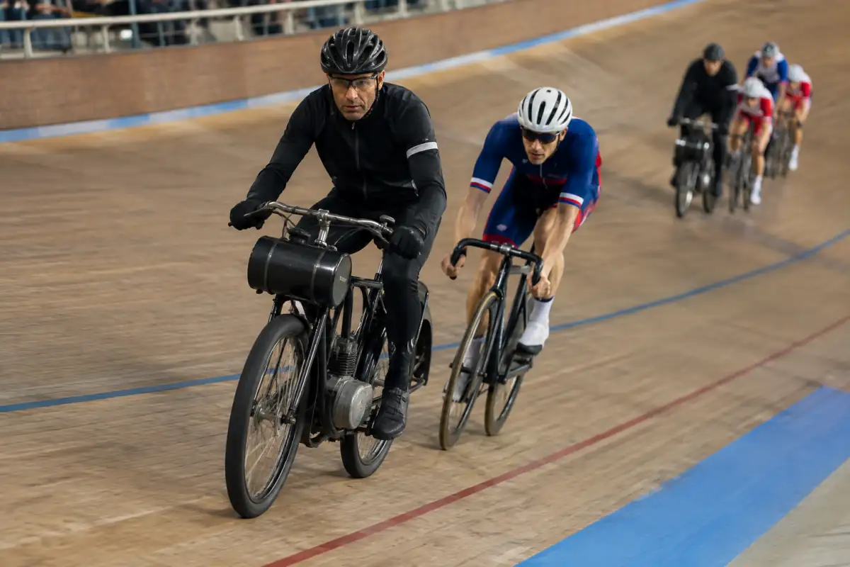 Course derrière derny sur un vélodrome : des cyclistes en tenue de piste suivent de près un pilote motorisé dans le virage.