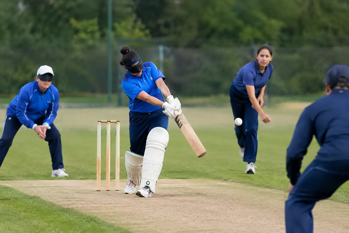 Un frappeur joue une balle sonore à la batte lors d’un match de cricket pour aveugles sur un terrain extérieur.