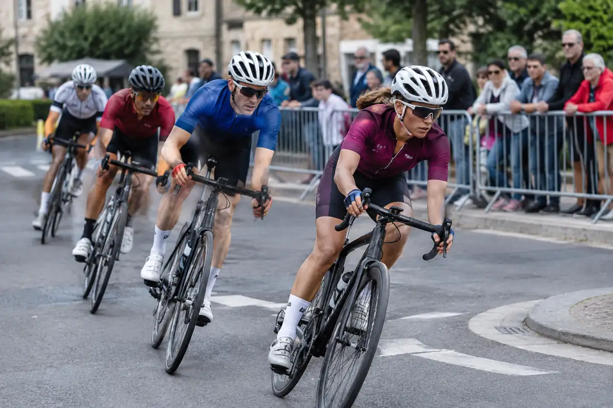 Peloton de coureurs négociant un virage lors d’un critérium cycliste sur un circuit urbain fermé en France.