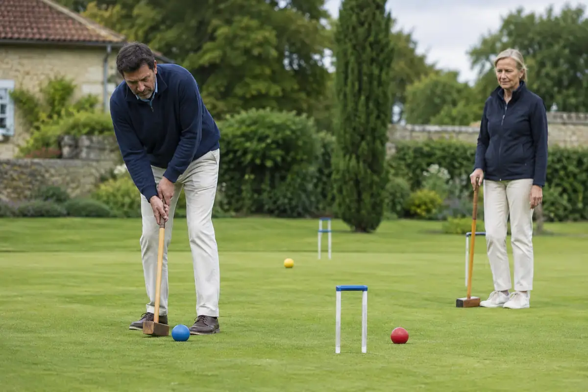Joueurs de croquet sur une pelouse, alignant maillet et boule pour viser un arceau métallique.