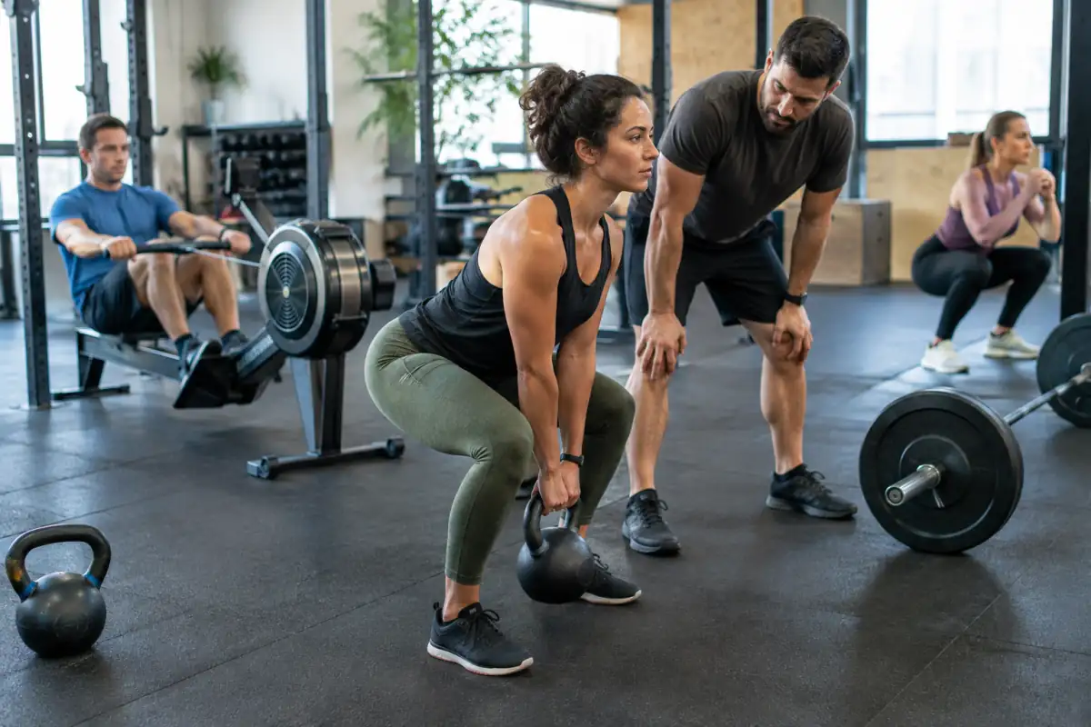 Séance de cross-training en salle : une pratiquante réalise un soulevé de kettlebell sous l’œil d’un coach.