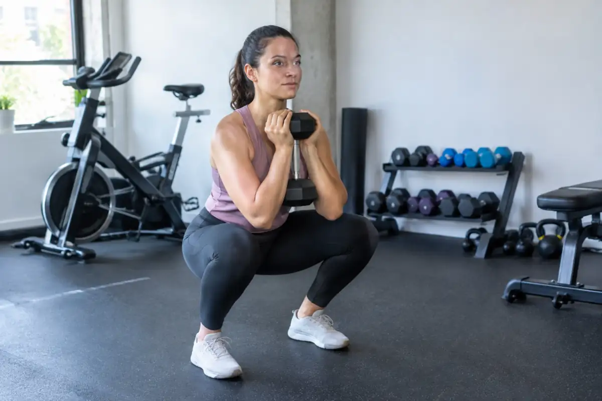 Débutant réalisant un squat gobelet contrôlé avec un haltère dans une séance équilibrant renforcement et cardio.