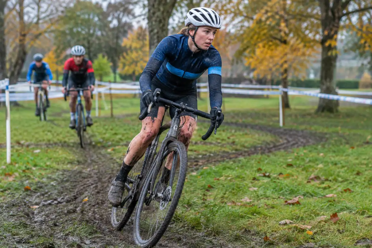 Un coureur de cyclo-cross relance son vélo à guidon courbé dans un virage boueux sur un circuit herbeux d’automne.