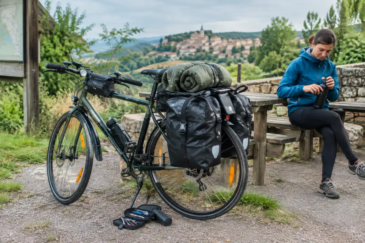 Vélo de randonnée chargé de sacoches étanches, avec éclairage, kit de réparation et veste de pluie prêts pour une sortie.