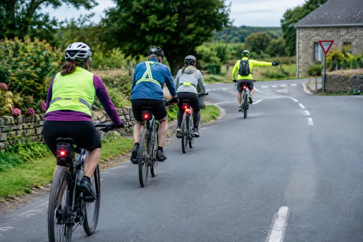 Cyclistes en randonnée sur une route de campagne, espacés en file simple, avec un participant qui signale un changement de direction.