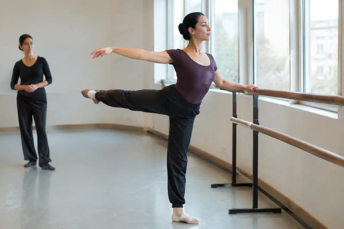 Une danseuse débutante travaille son équilibre près de la barre avant un cours, dans une posture contrôlée et sans forcer.