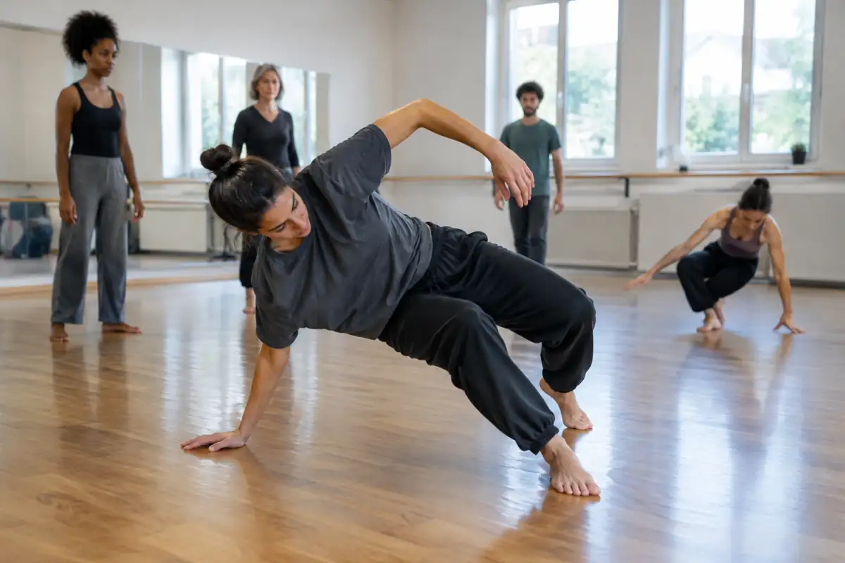 Danseuse en cours de danse contemporaine, contrôlant une transition debout vers le sol dans un studio lumineux.