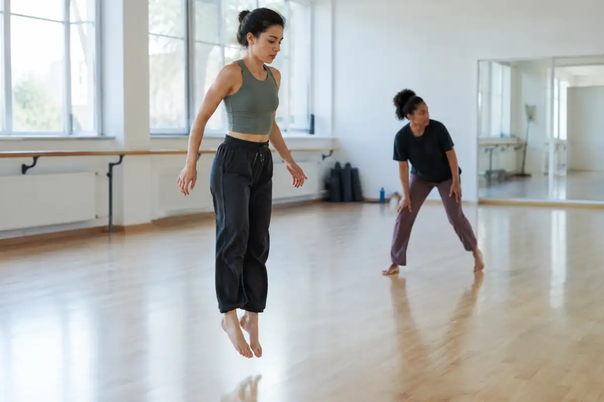 En studio, une danseuse contemporaine répète un petit saut avec une réception souple sur un plancher dégagé.