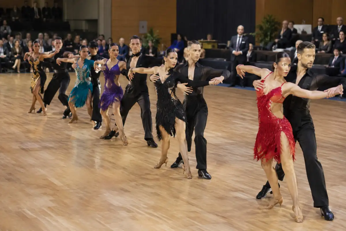 Équipe de danse en formation exécutant une chorégraphie latine synchronisée sur un parquet de compétition.