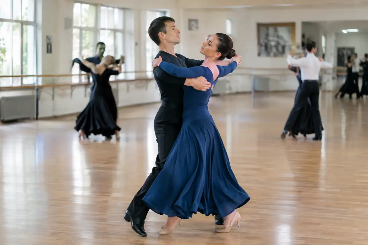 Un couple exécute une valse anglaise en tenue de danse sportive standard sur le parquet d’une salle de cours.