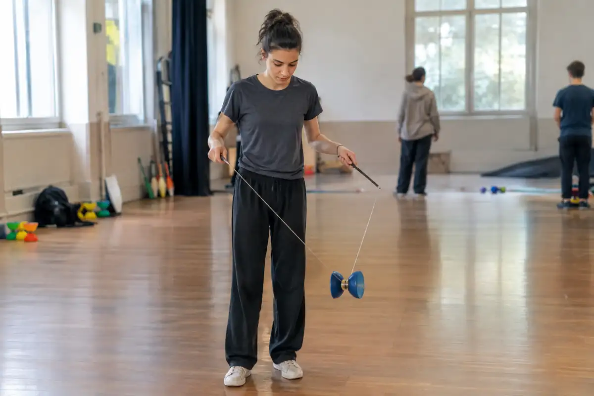 Un jongleur fait tourner et lance un diabolo entre deux baguettes dans une salle de pratique de cirque.