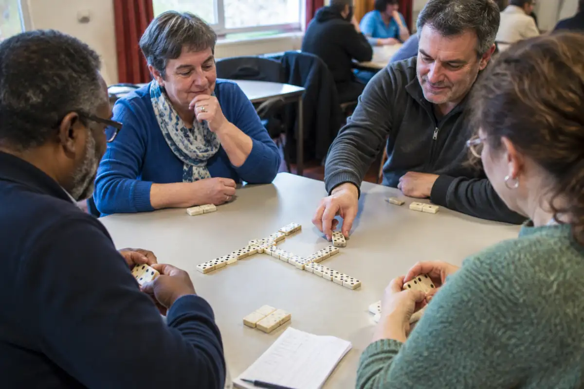 Joueurs concentrés autour d’une table lors d’une partie de dominos de compétition en équipes, avec les pièces et le score.