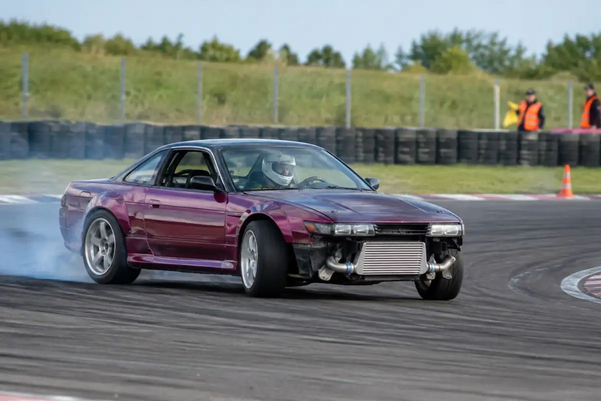 Une voiture de drift à propulsion glisse en contre-braquage dans un virage balisé sur un circuit fermé.