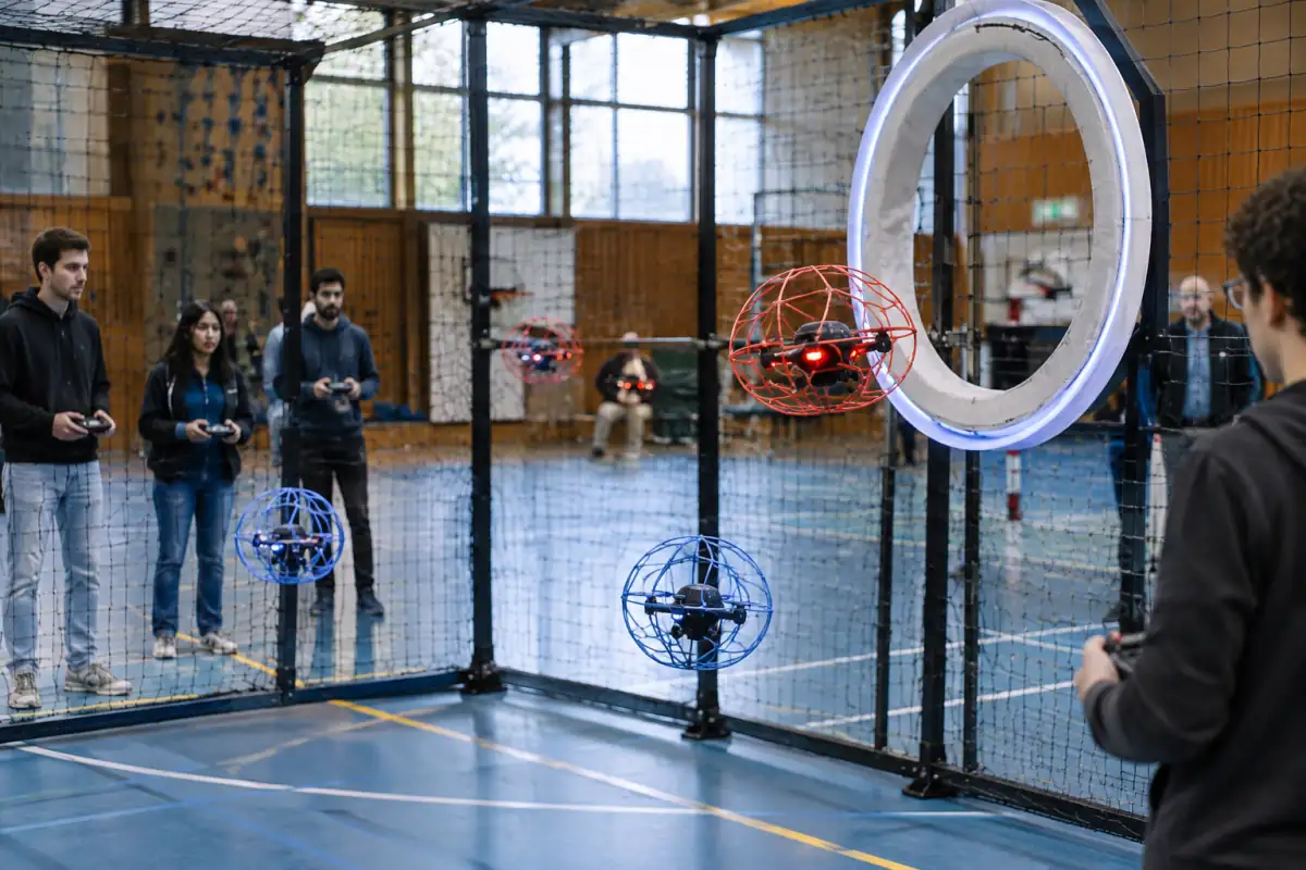 Match de drone soccer en salle : un drone protégé approche de l’anneau de but pendant que les pilotes dirigent leurs appareils.