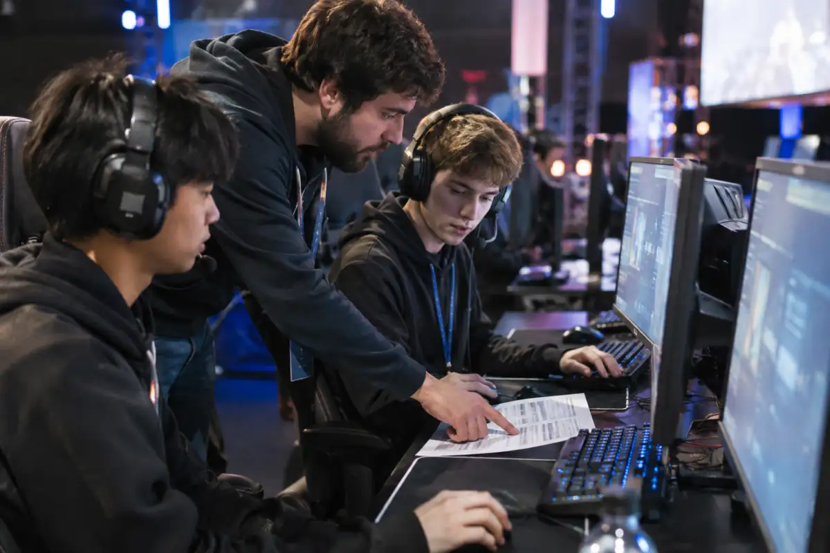 Joueurs et coach consultent le tableau d’un tournoi d’e-sport dans une salle de compétition en réseau local.