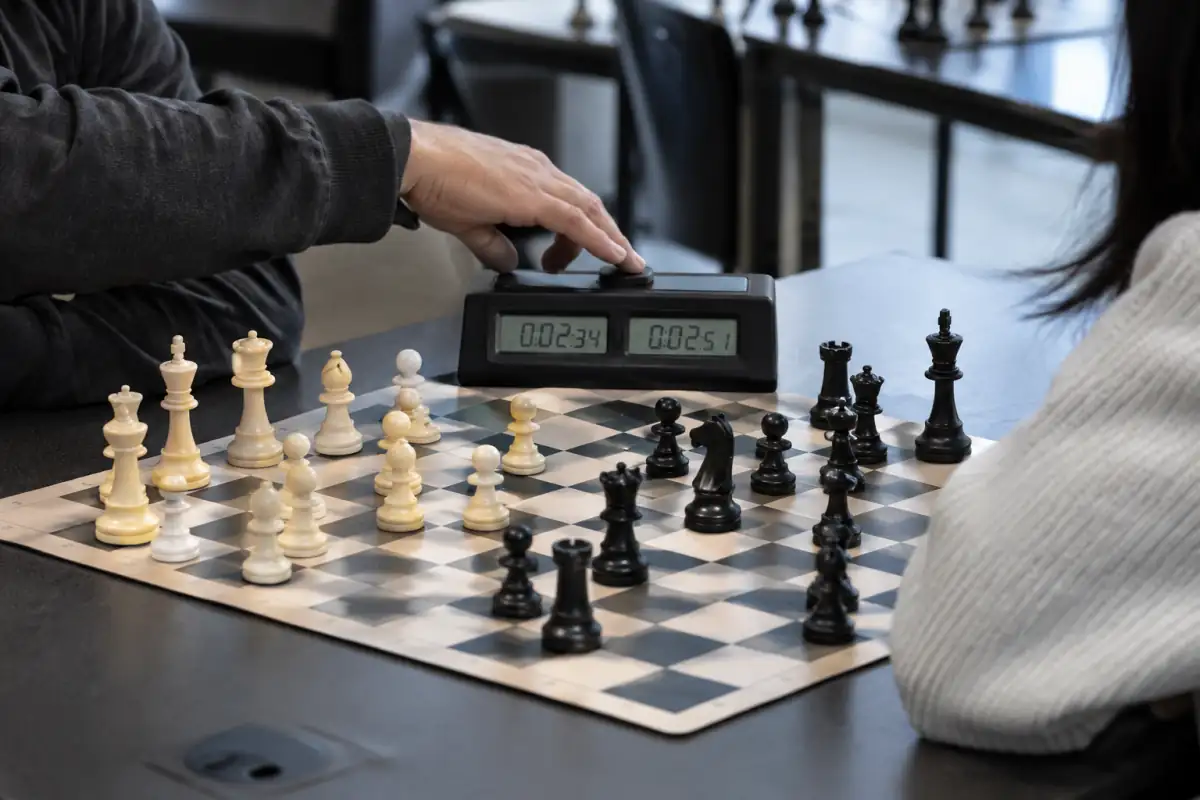 Pendule numérique à côté d’un échiquier de tournoi et de pièces Staunton, avec un joueur qui appuie sur son bouton après un coup.