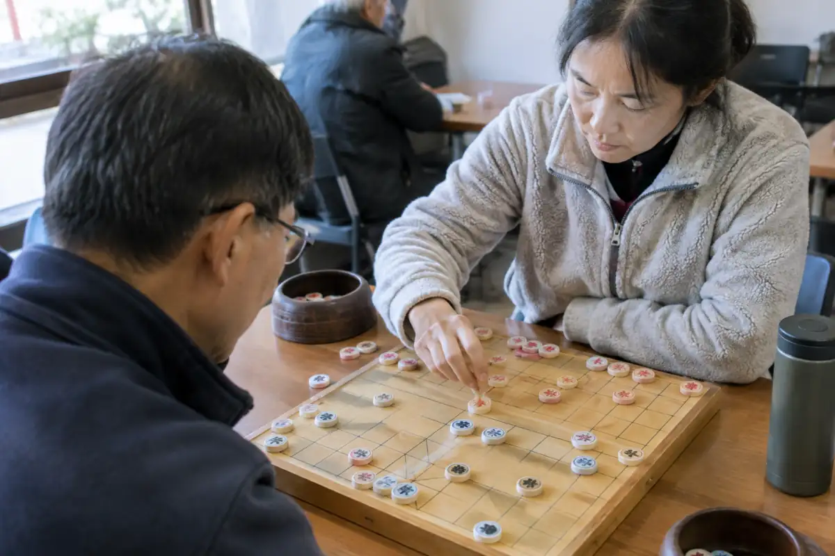 Partie de janggi sur un plateau coréen quadrillé, avec des pièces rondes déplacées par deux joueurs concentrés.