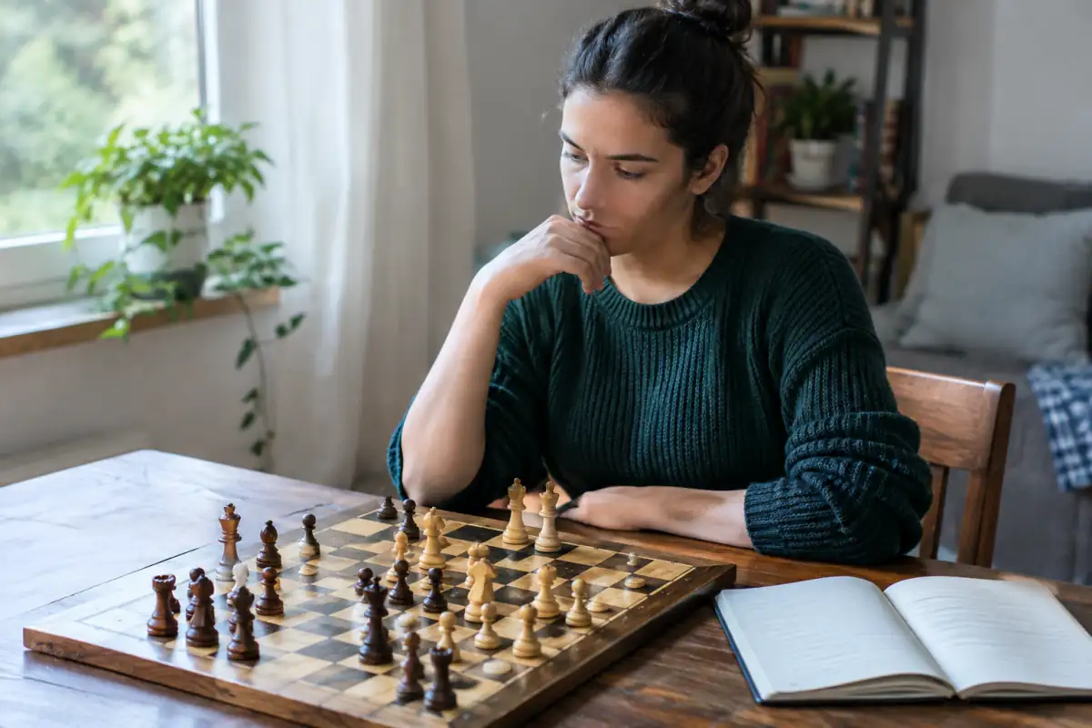 Débutant aux échecs qui réfléchit à une position tactique devant un échiquier, un carnet posé à côté pour noter ses erreurs.