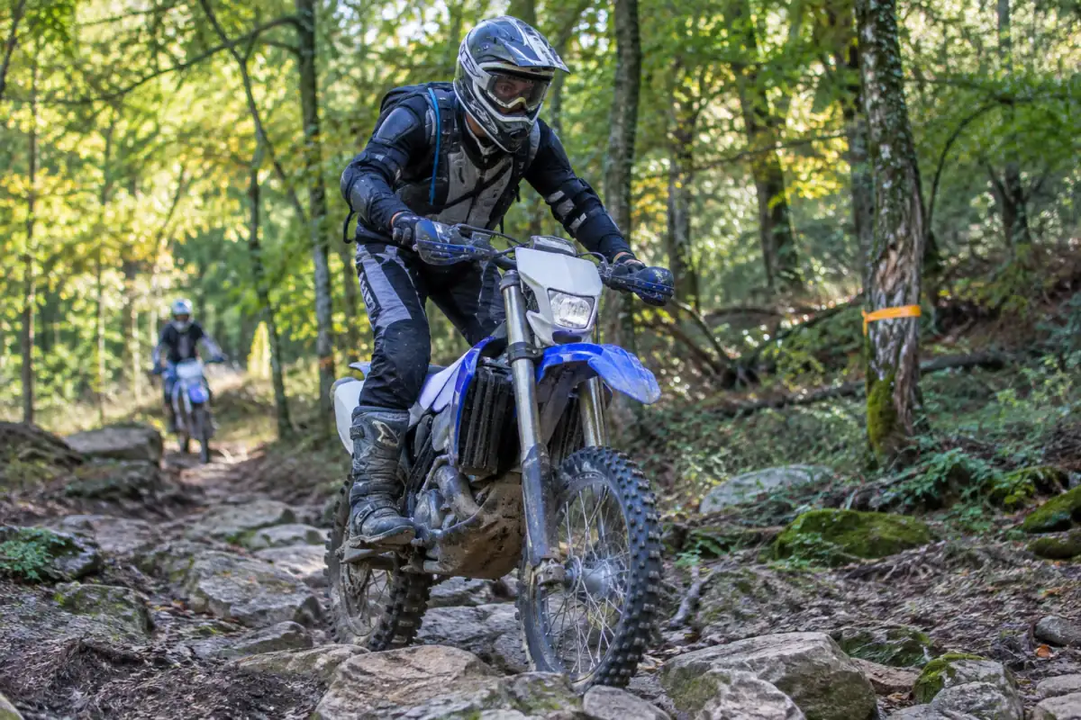 Pilote en tenue de protection franchissant un passage rocheux à moto lors d’une séance d’enduro en forêt.