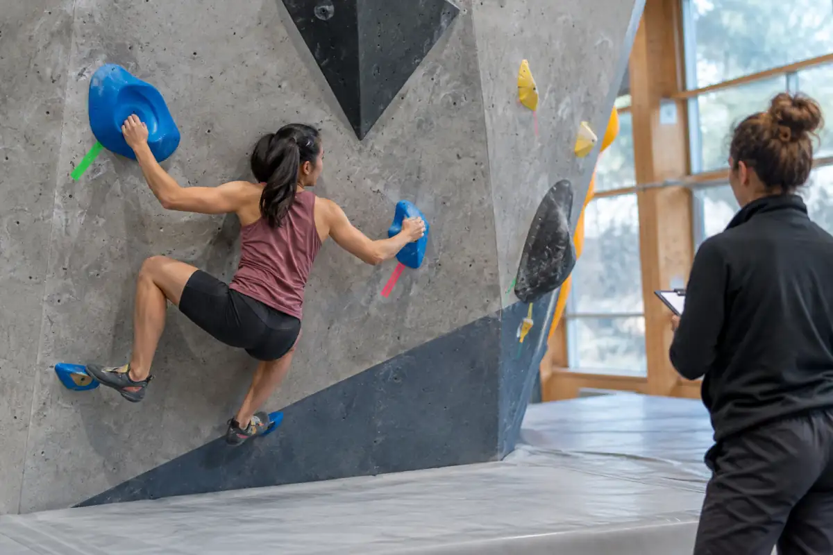 Départ d’un bloc en compétition : mains sur les prises marquées, pieds en position et tapis dégagé sous le grimpeur.