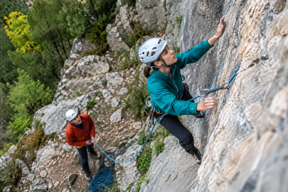 Deux grimpeurs en escalade de grandes voies sur une falaise calcaire ; le leader clippe une dégaine tandis que son partenaire l’assure.