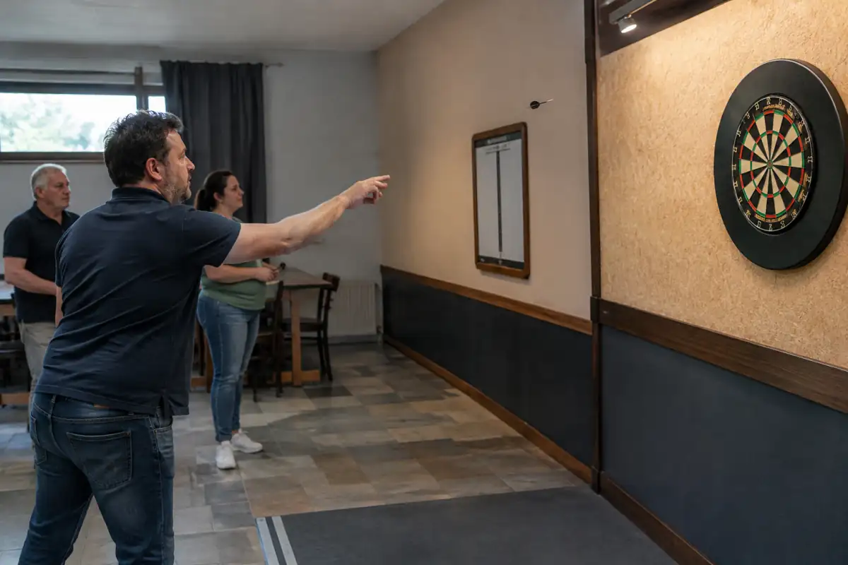 Une joueuse lance une fléchette à pointe acier vers une cible traditionnelle dans une salle de club, tandis que les autres attendent derrière la ligne.