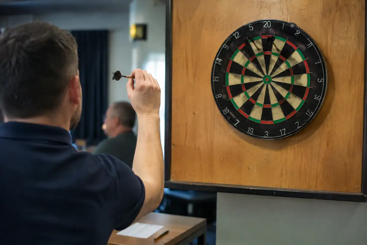 Joueur de fléchettes préparant une sortie au double devant une cible réglementaire, avec une feuille de score posée à proximité.