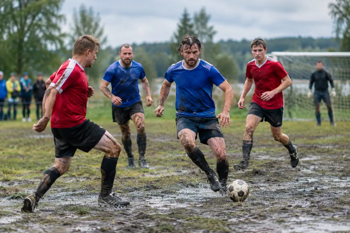 Des joueurs disputent un match de football des marais sur un terrain boueux, en adaptant leurs appuis et leurs passes.