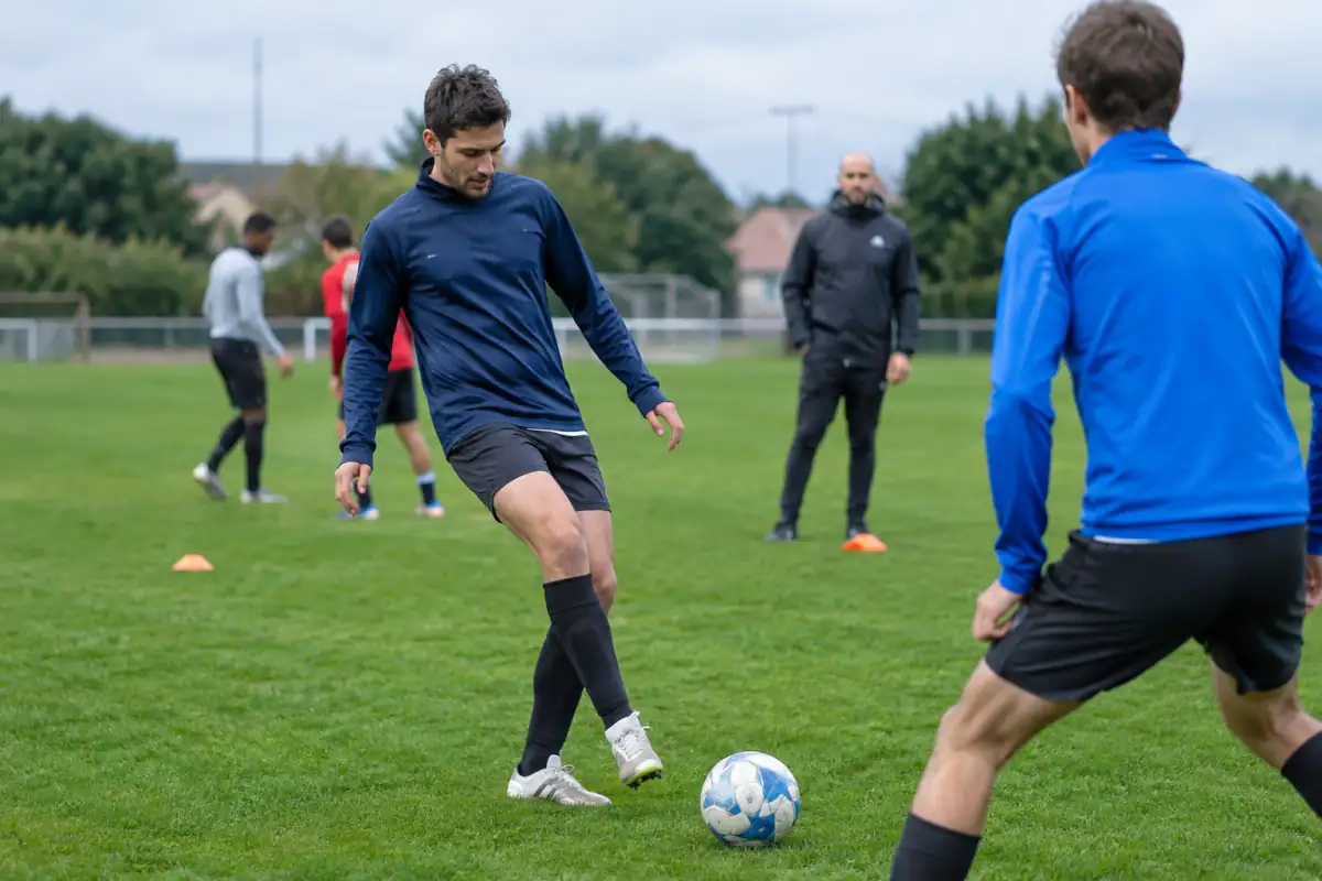 Un adulte débutant travaille une passe courte avec un partenaire lors d’une séance d’essai de football en club.