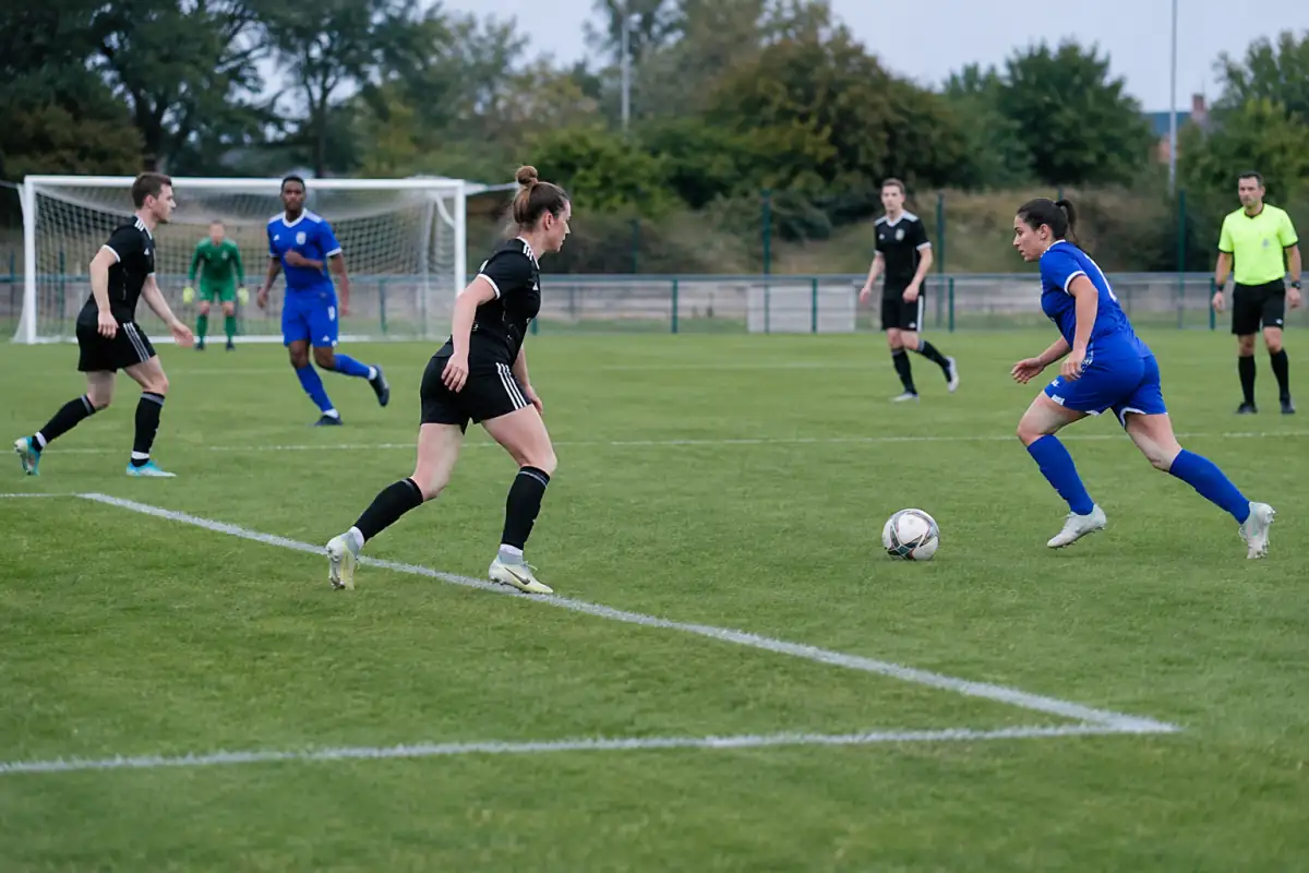 Un attaquant déclenche son appel face à une ligne défensive pendant qu’un arbitre observe une action de hors-jeu sur un terrain de football.