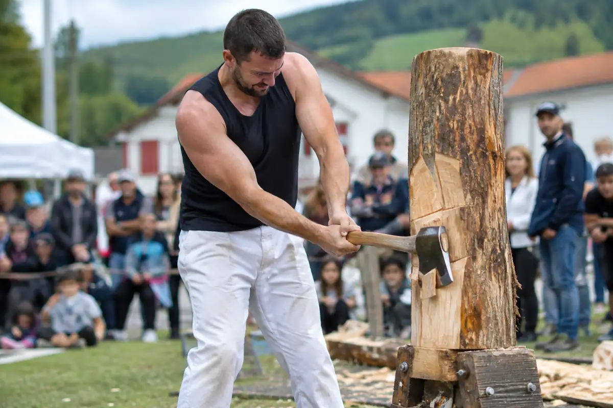 Un athlète pratique la force basque en fendant à la hache un tronc dressé sur un support lors d’une épreuve en plein air.