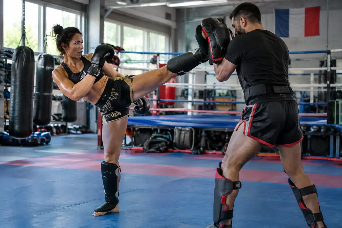 Deux pratiquants travaillent un coup de pied circulaire au-dessus de la ceinture lors d’un entraînement de full-contact en salle.