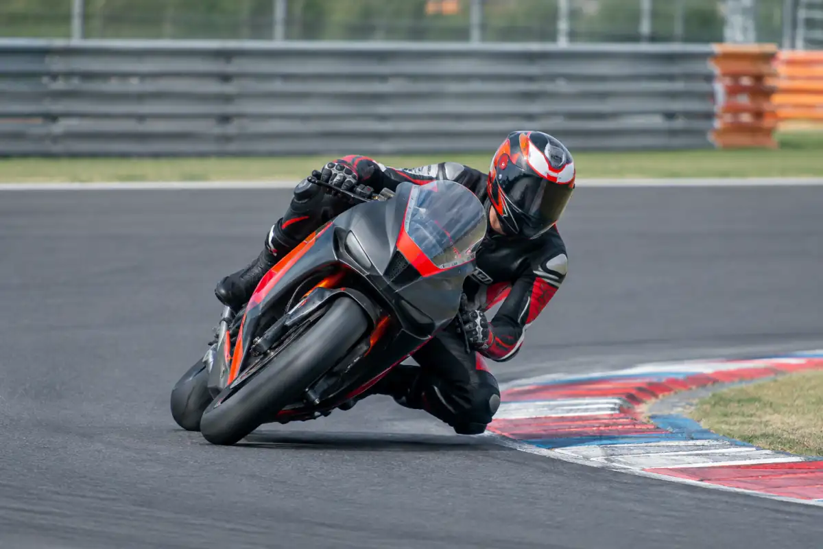 Pilote de Grand Prix moto en combinaison cuir, incliné dans un virage sur un circuit fermé avec sa moto prototype.