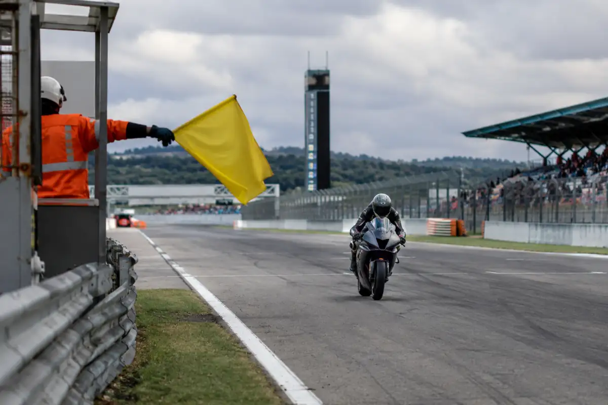 Pilote MotoGP en qualification approche d’un poste de commissaire présentant un drapeau jaune au bord du circuit.