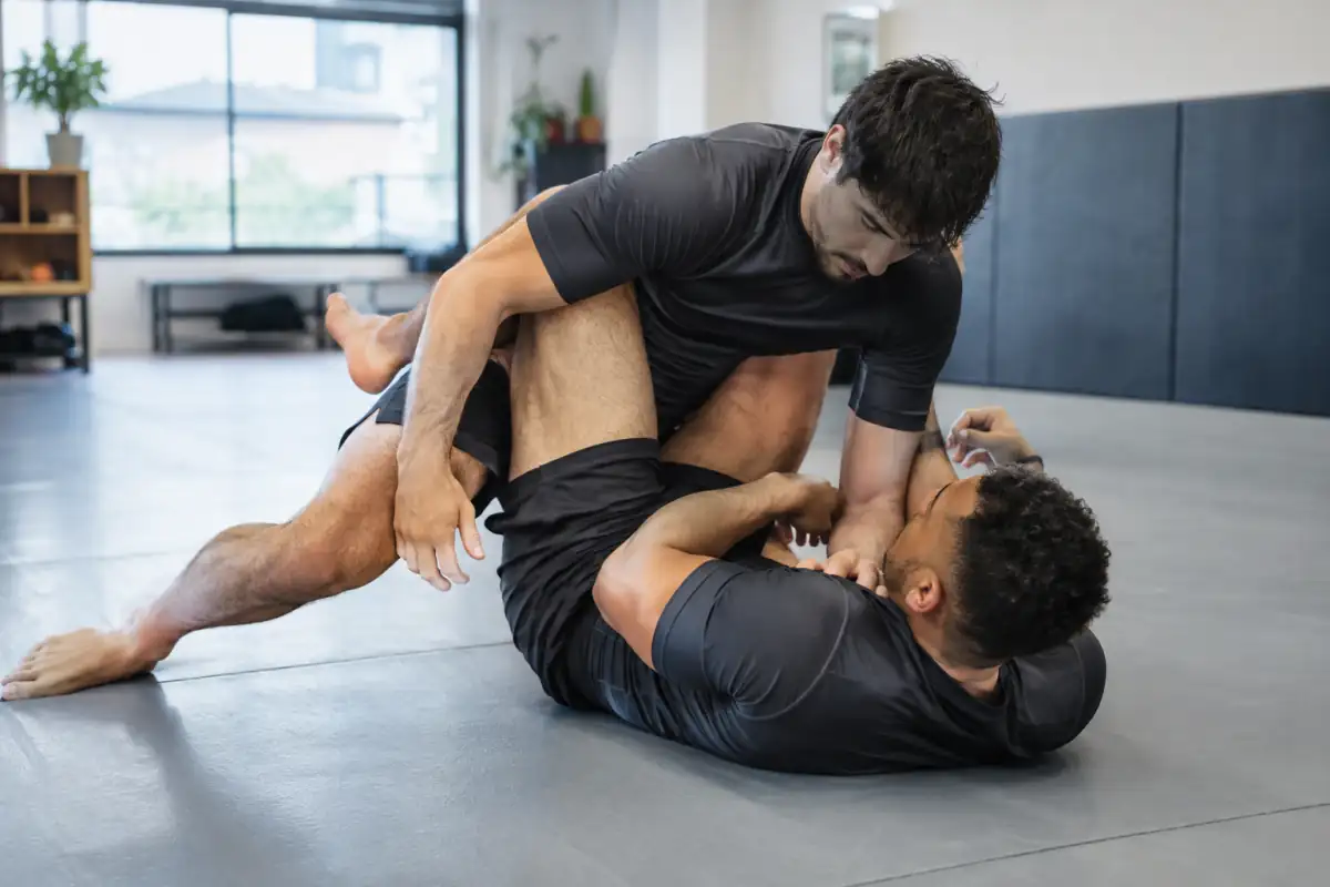 Deux pratiquants en rashguard travaillent un passage de garde en grappling no-gi sur le tapis d’une salle.