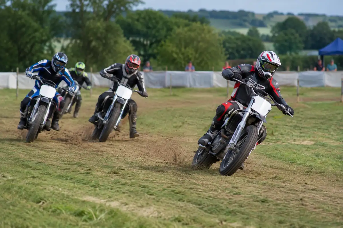 Pilotes de grass track moto en peloton dans un virage sur un circuit temporaire tracé sur l’herbe.