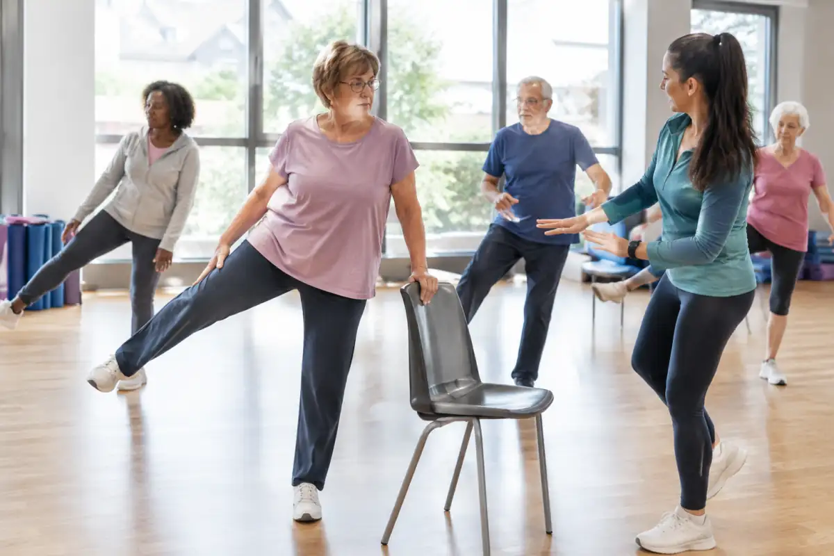Un groupe d’adultes pratique la gymnastique douce en salle avec des exercices contrôlés d’équilibre et de mobilité.
