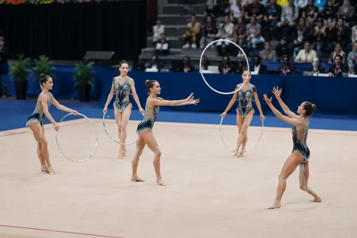 Cinq gymnastes rythmiques réalisent un échange de cerceaux synchronisé sur le praticable pendant un exercice en ensemble.