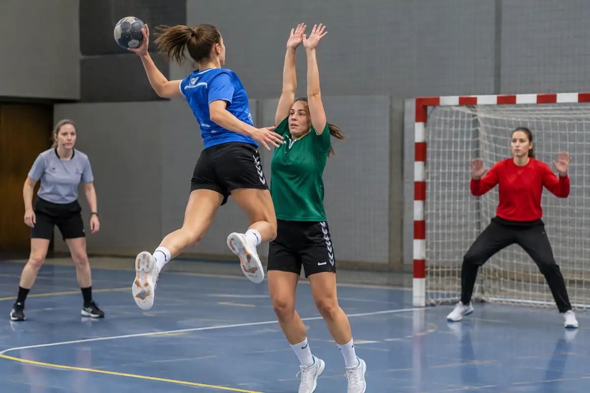 Tir en suspension au handball : l’attaquant lâche le ballon avant de retomber dans la zone des 6 mètres, sous le regard de l’arbitre.