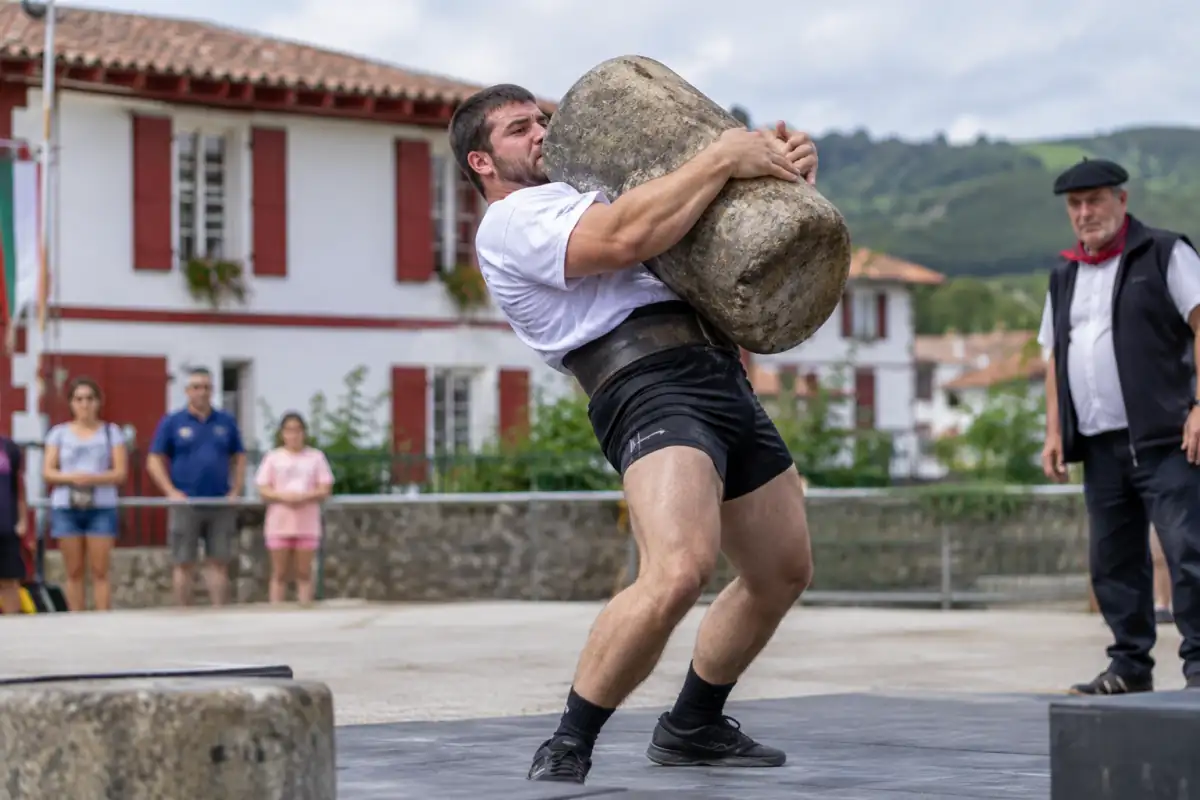 Un harrijasotzaile soulève une pierre cylindrique contre son épaule lors d’une épreuve de lever de pierre basque.