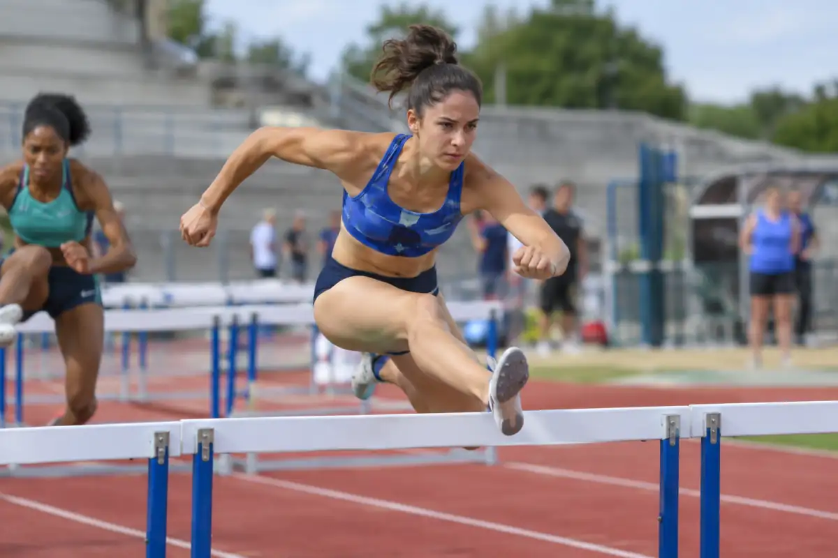 Une heptathlète franchit une haie sur la piste lors d’une compétition d’athlétisme en plein air.