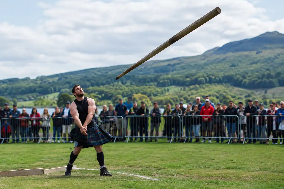 Un athlète lance un caber pendant des Highland games, sur un terrain extérieur, devant des spectateurs maintenus à distance.