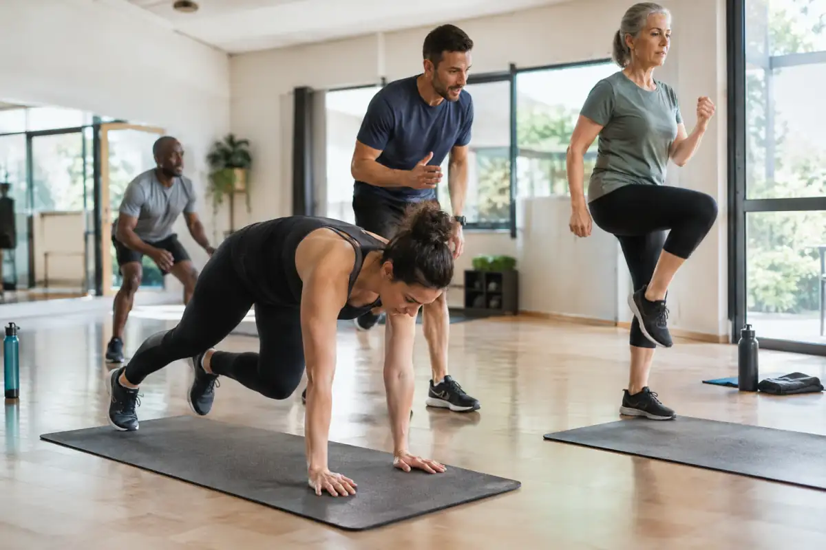 Séance de HIIT en salle : une pratiquante réalise un squat thrust pendant qu’un coach observe le mouvement.