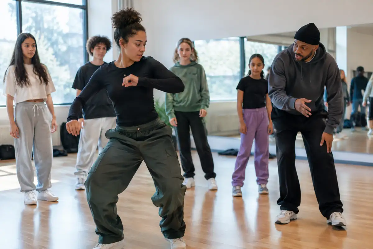Un cours de danse hip-hop en studio où une personne travaille un groove debout devant un petit groupe attentif.